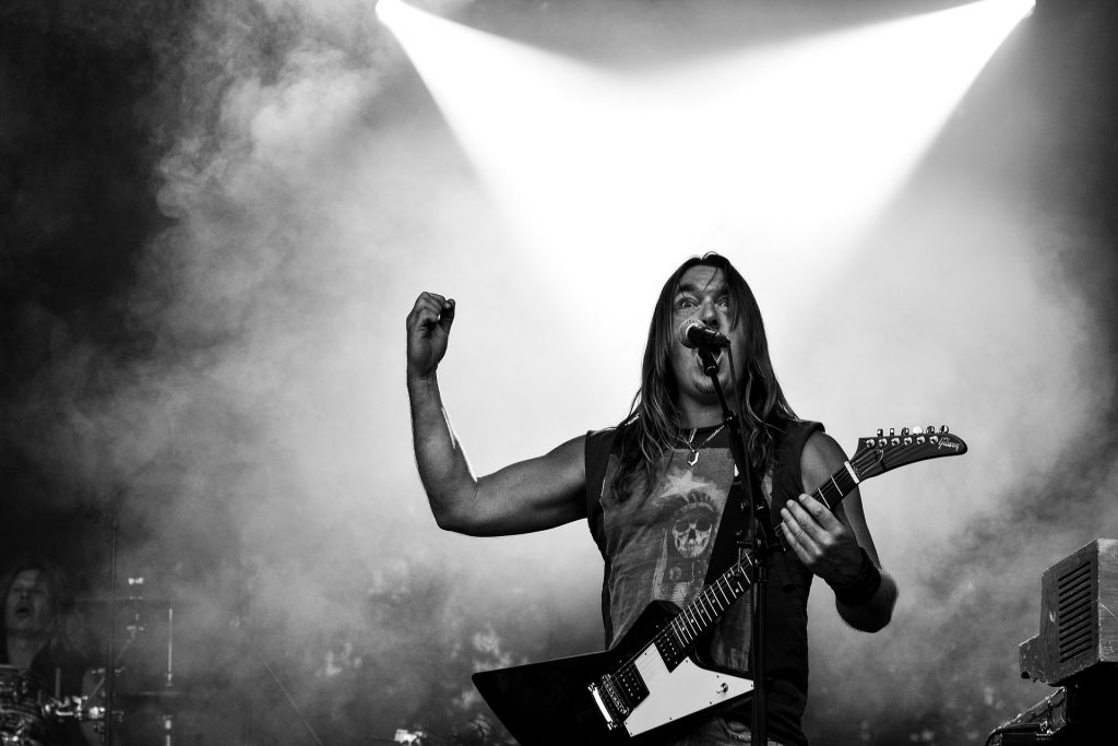 Male rock vocalist belts out a note with his guitar in hand. 